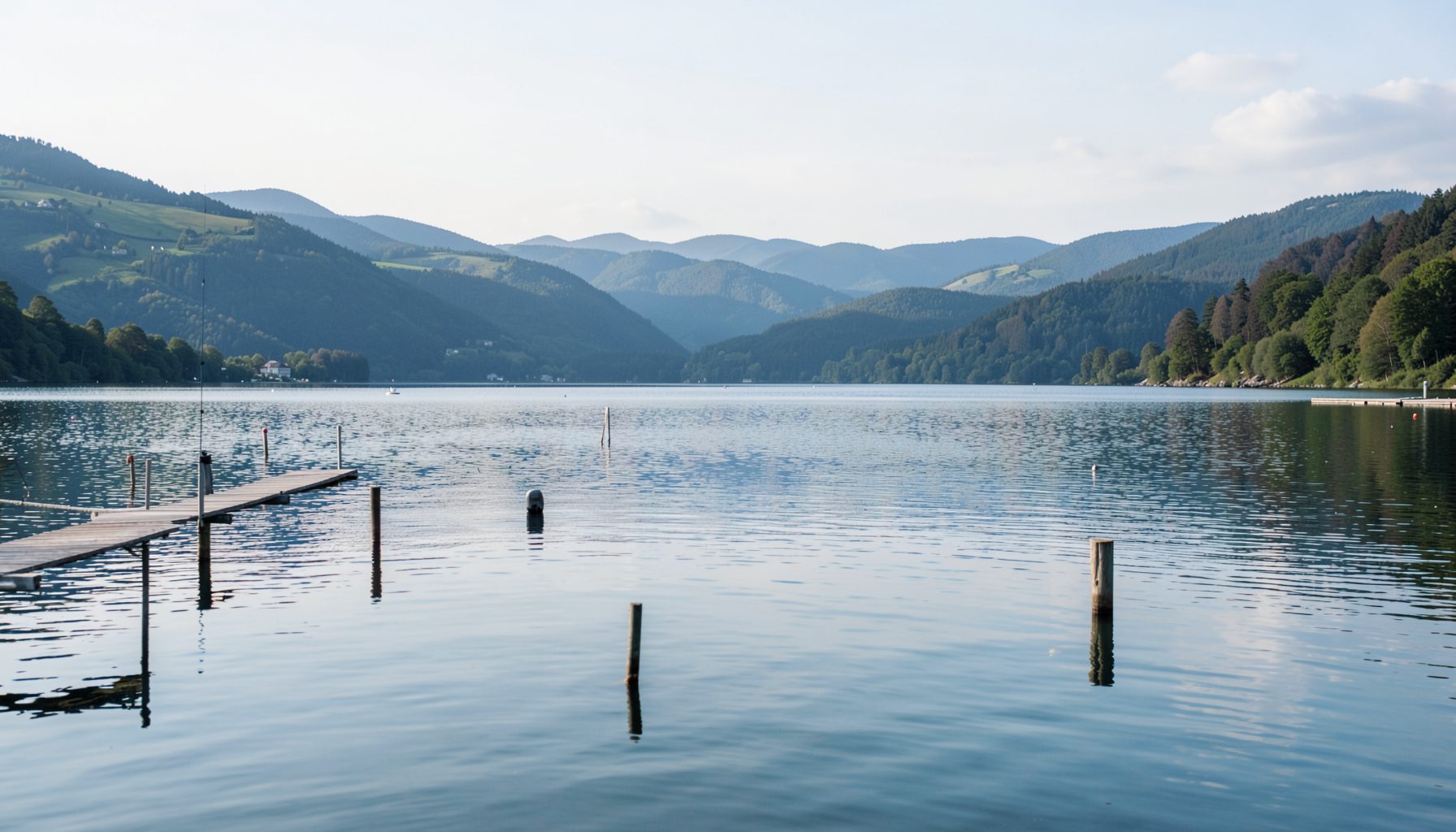 Seeblick mit ruhigem Wasser, Bootssteg und sanften Hügeln im Hintergrund
